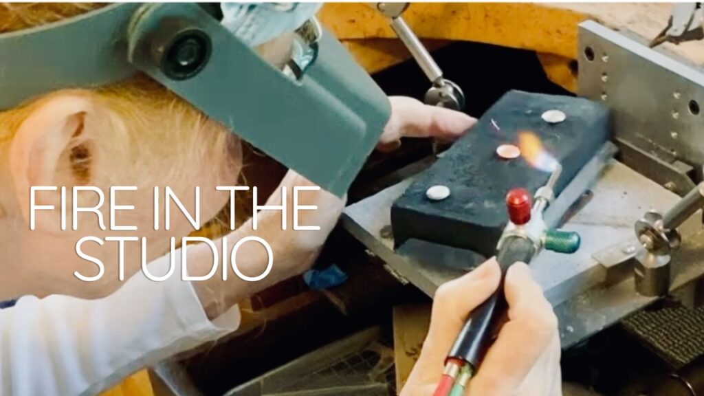 craftswoman working with torch at bench making jewelry